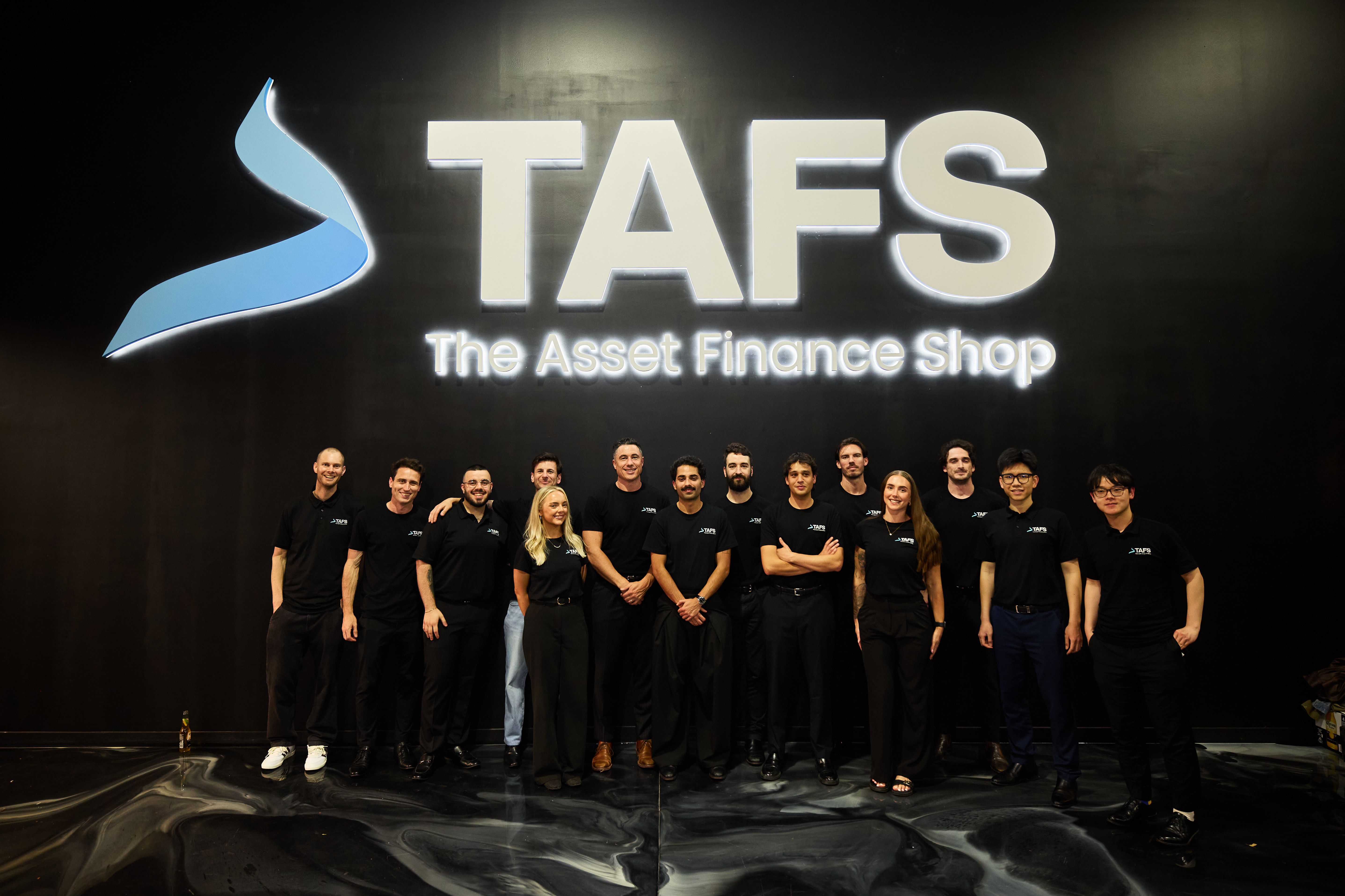 The TAFS team standing together in front of the illuminated TAFS sign.